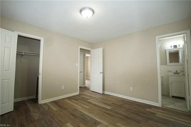 unfurnished bedroom featuring a closet, baseboards, wood finished floors, ensuite bathroom, and a sink