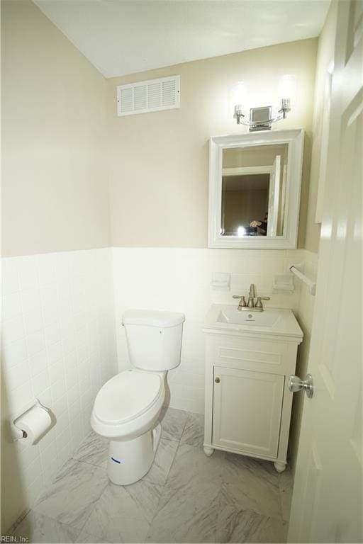 bathroom featuring marble finish floor, tile walls, visible vents, toilet, and vanity