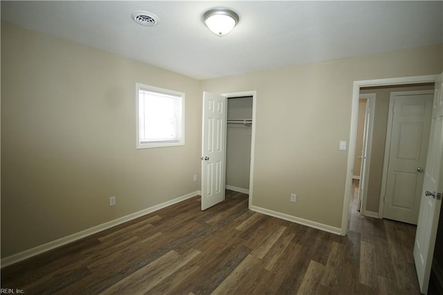 unfurnished bedroom with a closet, dark wood finished floors, visible vents, and baseboards