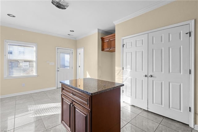 kitchen with a center island, light tile patterned floors, ornamental molding, dark stone countertops, and baseboards