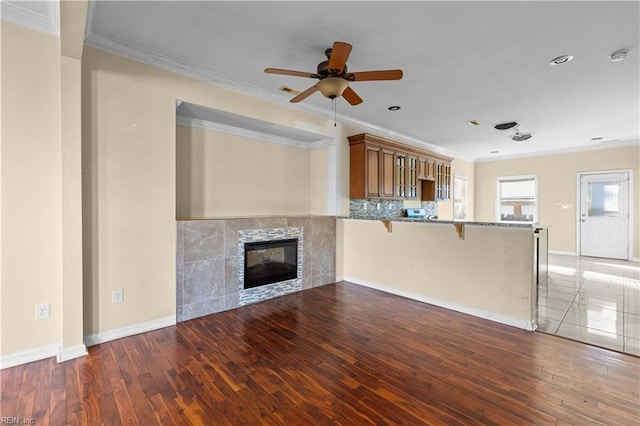 unfurnished living room featuring ornamental molding, a ceiling fan, wood finished floors, a tile fireplace, and baseboards