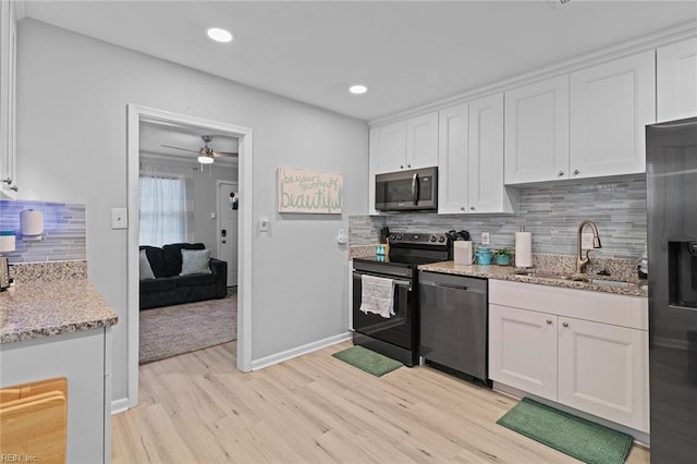 kitchen with light stone counters, light wood-style flooring, stainless steel appliances, a sink, and white cabinetry