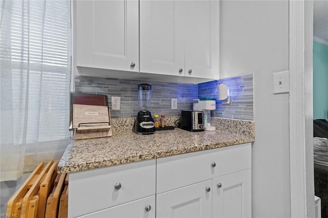 kitchen featuring tasteful backsplash, light stone counters, and white cabinets