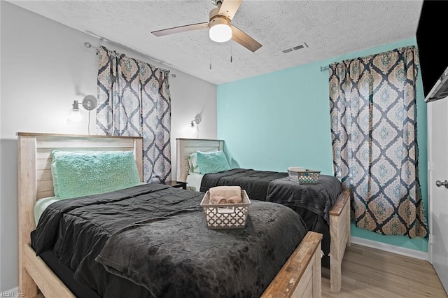 bedroom featuring light wood-type flooring, a ceiling fan, visible vents, and a textured ceiling