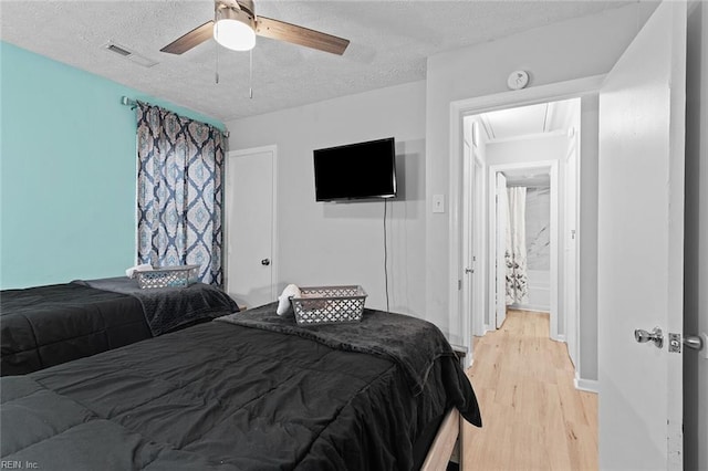 bedroom with a textured ceiling, ceiling fan, light wood finished floors, and visible vents