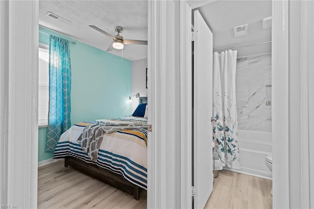 bedroom featuring ceiling fan, a textured ceiling, visible vents, and wood finished floors