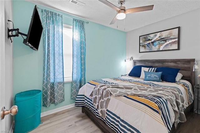 bedroom with a textured ceiling, wood finished floors, visible vents, baseboards, and a ceiling fan