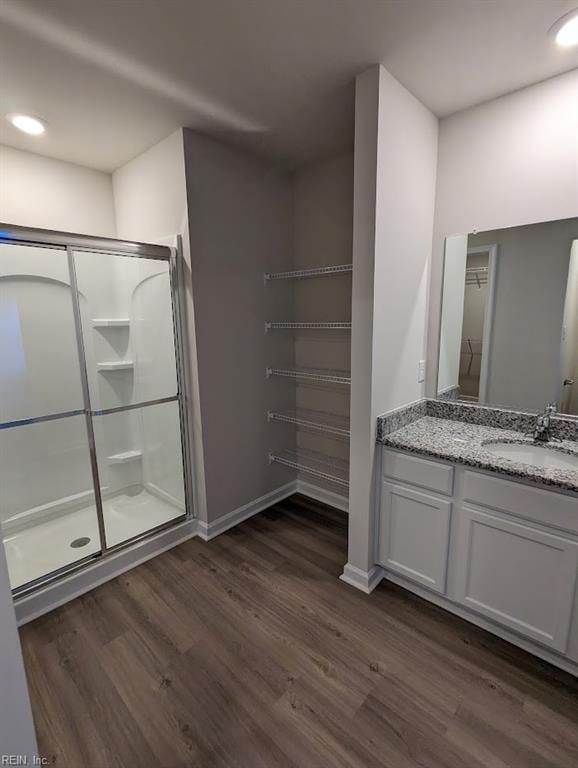 full bathroom featuring a spacious closet, vanity, a shower stall, wood finished floors, and baseboards