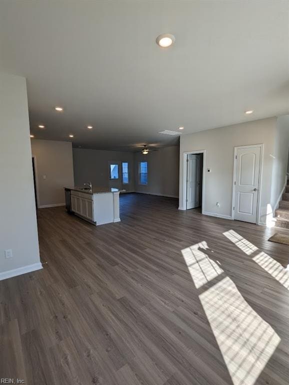 unfurnished living room featuring recessed lighting, dark wood-style flooring, a sink, baseboards, and stairs