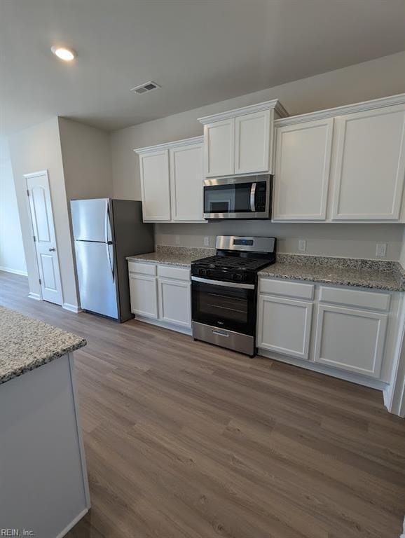 kitchen with appliances with stainless steel finishes, wood finished floors, visible vents, and white cabinetry