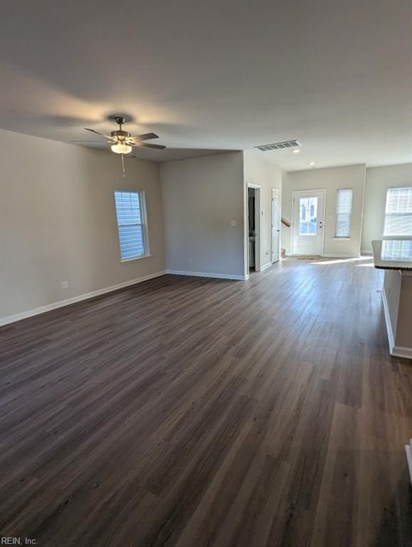 unfurnished living room featuring dark wood-type flooring, visible vents, and baseboards