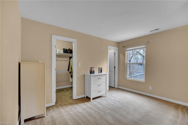 unfurnished bedroom with a closet, light colored carpet, visible vents, a spacious closet, and baseboards