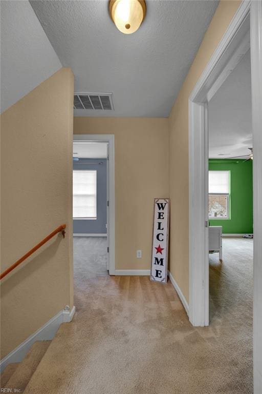 corridor with an upstairs landing, carpet flooring, visible vents, and baseboards