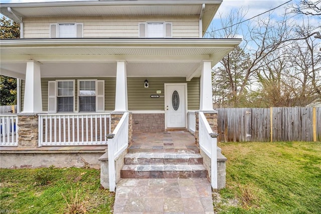 entrance to property with stone siding, a yard, a porch, and fence