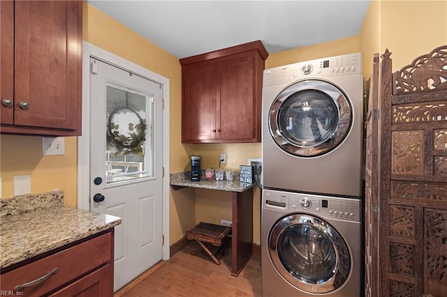 clothes washing area with stacked washer / dryer, cabinet space, light wood-style flooring, and baseboards