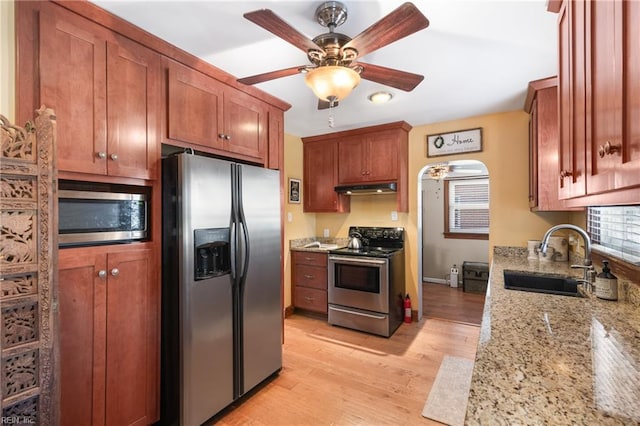 kitchen with stainless steel appliances, light wood-style flooring, a ceiling fan, a sink, and under cabinet range hood