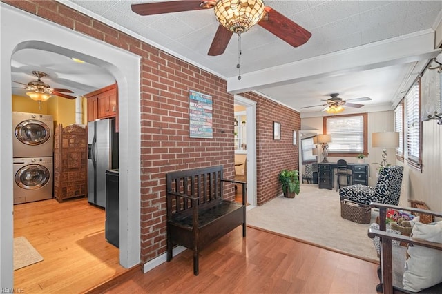 interior space featuring stacked washer and dryer, ornamental molding, brick wall, light wood-type flooring, and stainless steel fridge with ice dispenser