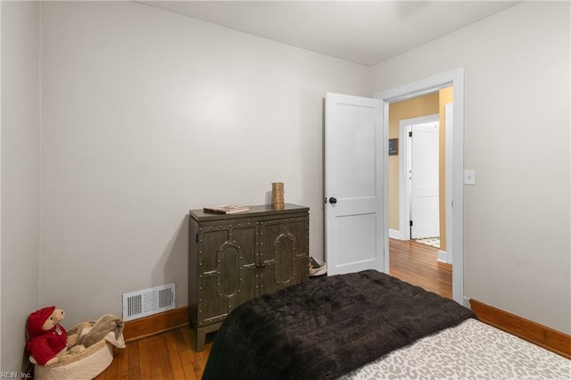 bedroom with hardwood / wood-style floors, visible vents, and baseboards