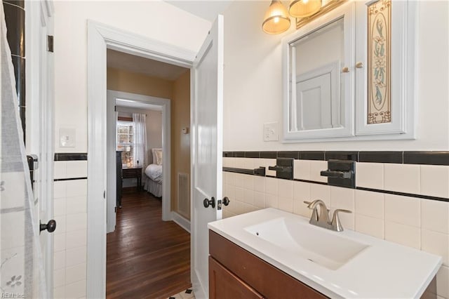 bathroom with a wainscoted wall, tile walls, visible vents, vanity, and wood finished floors