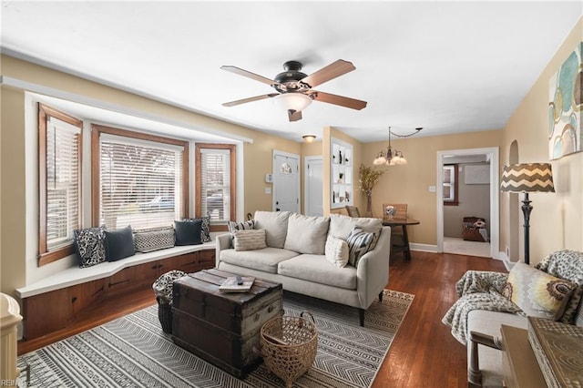 living area featuring baseboards, dark wood-type flooring, and ceiling fan with notable chandelier