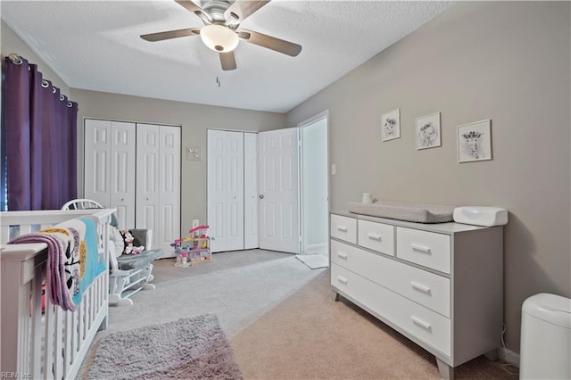 bedroom featuring multiple closets, light colored carpet, a textured ceiling, and a ceiling fan