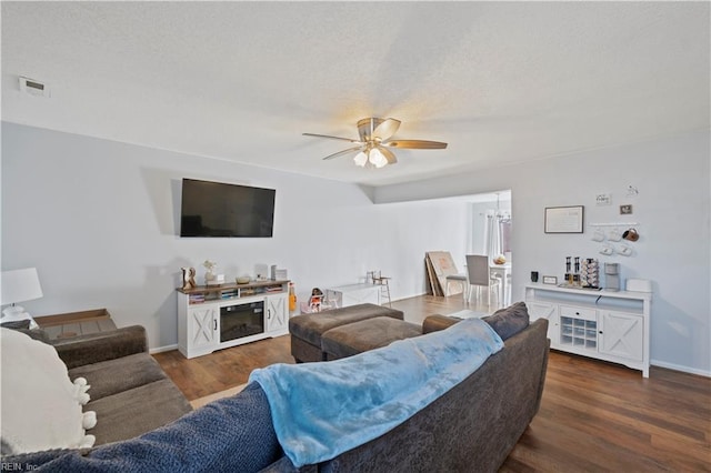 living area with ceiling fan with notable chandelier, dark wood finished floors, visible vents, and baseboards