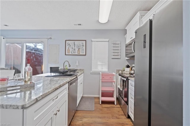 kitchen with light wood finished floors, visible vents, appliances with stainless steel finishes, white cabinets, and a peninsula