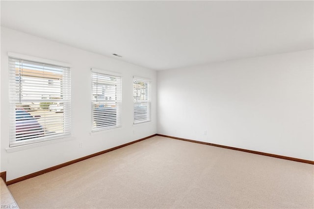 spare room with baseboards and light colored carpet