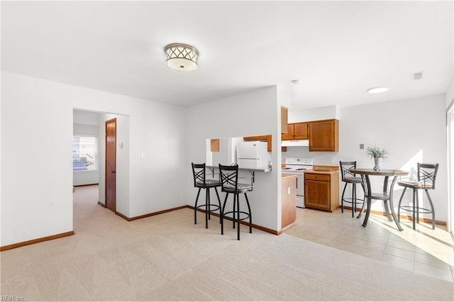 kitchen with brown cabinets, light colored carpet, white appliances, under cabinet range hood, and a kitchen breakfast bar