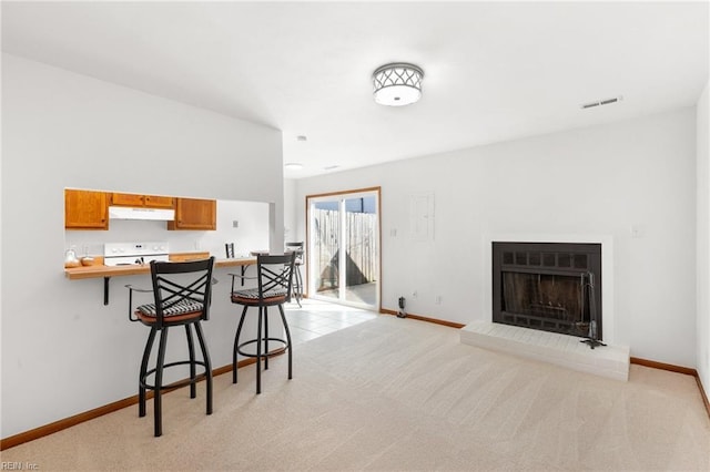 kitchen with light carpet, visible vents, a breakfast bar, under cabinet range hood, and white range with electric cooktop