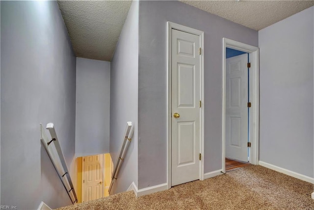 stairway featuring a textured ceiling, carpet floors, and baseboards