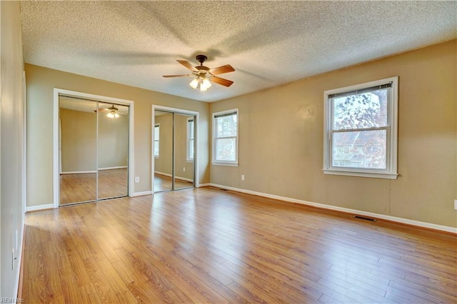 unfurnished bedroom featuring multiple closets, visible vents, baseboards, and wood finished floors