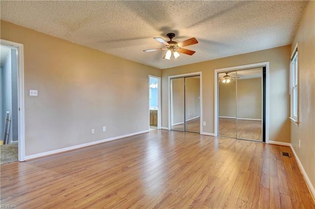 unfurnished bedroom with light wood-style flooring, baseboards, and two closets