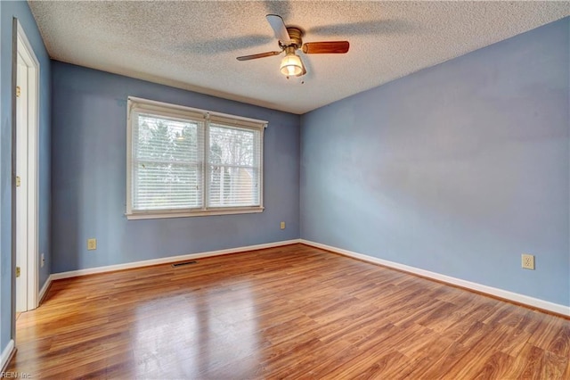 empty room featuring baseboards, visible vents, a ceiling fan, wood finished floors, and a textured ceiling