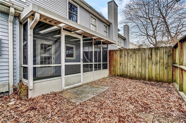 view of home's exterior featuring a sunroom, fence, and a chimney