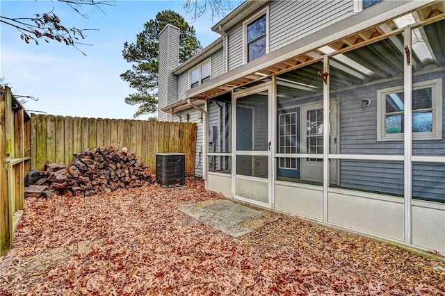 view of property exterior featuring a sunroom, a chimney, central AC unit, and fence