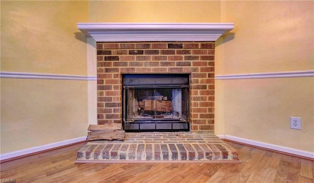 details featuring a brick fireplace, wood finished floors, and baseboards