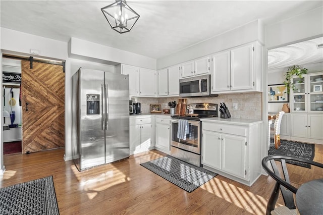 kitchen featuring stainless steel appliances, light countertops, light wood-style flooring, decorative backsplash, and a barn door