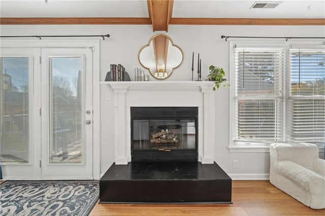 living area featuring baseboards, visible vents, a glass covered fireplace, beamed ceiling, and wood finished floors