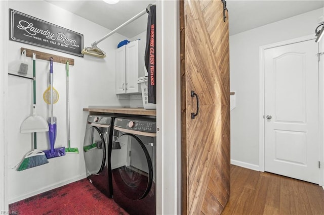 laundry area with a barn door, wood finished floors, baseboards, cabinet space, and washing machine and clothes dryer