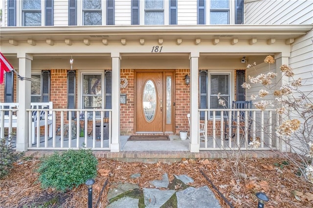 view of exterior entry with covered porch and brick siding