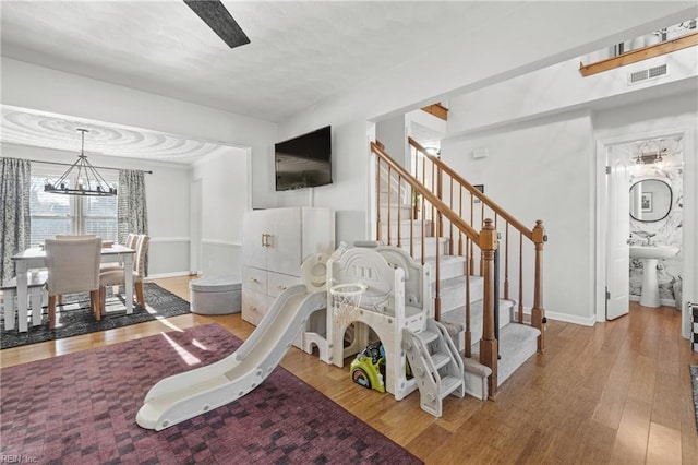 interior space featuring ceiling fan with notable chandelier, visible vents, baseboards, and wood finished floors