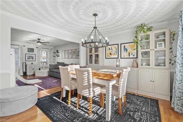 dining room with ornamental molding, wood finished floors, and ceiling fan with notable chandelier