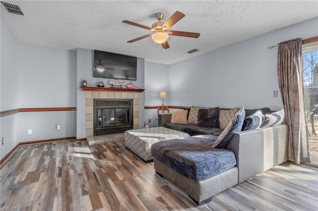 living area with a textured ceiling, ceiling fan, a fireplace, wood finished floors, and visible vents