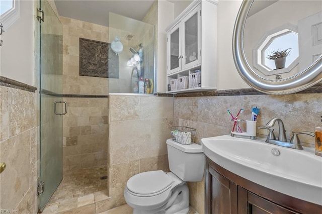 full bathroom with a stall shower, wainscoting, toilet, vanity, and tile walls