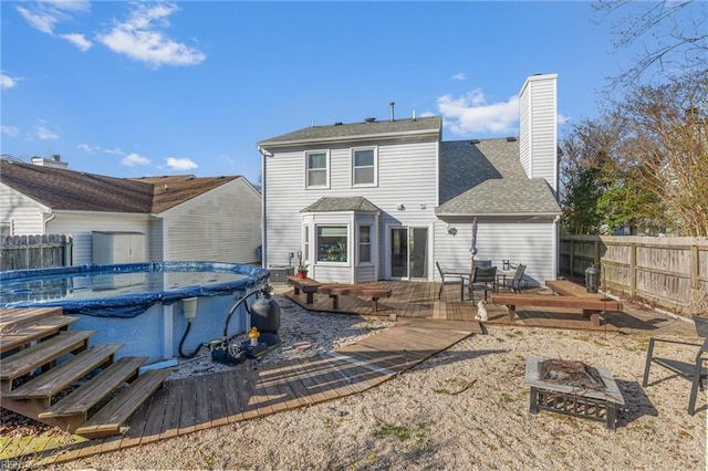 rear view of property with a deck, an outdoor fire pit, fence, a fenced in pool, and a chimney