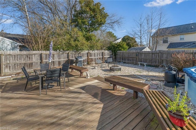 wooden deck featuring outdoor dining space, a fenced backyard, a fire pit, and area for grilling