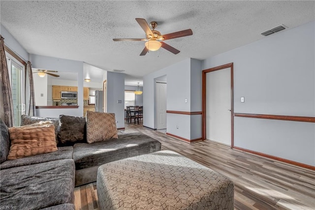 living room featuring visible vents, a ceiling fan, a textured ceiling, wood finished floors, and baseboards