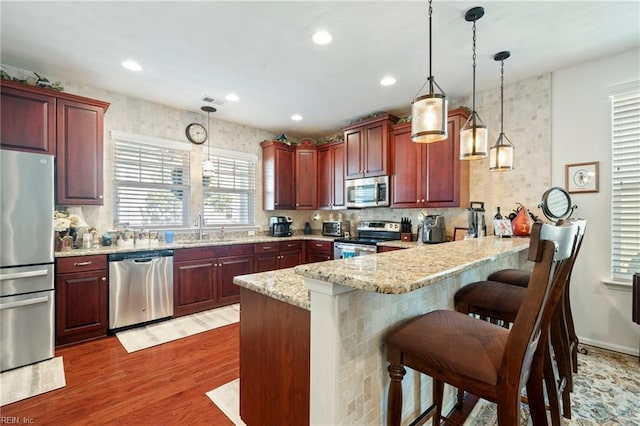 kitchen with wood finished floors, decorative light fixtures, a peninsula, stainless steel appliances, and a sink