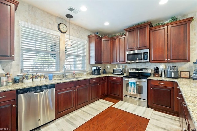 kitchen with stainless steel appliances, a sink, visible vents, dark brown cabinets, and hanging light fixtures